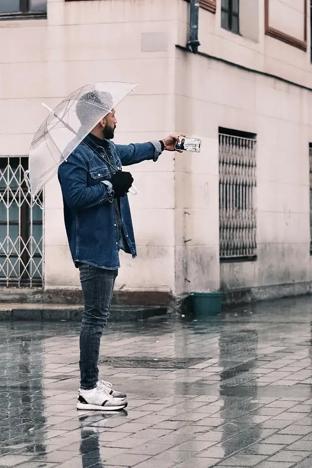 Man holding umbrella and taking selfie with his phone