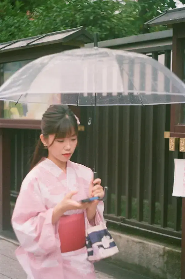 Woman holding umbrella in the rain, smiling at her phone